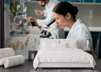 Concentrated young female scientist working with microscope in chemical lab Wall mural