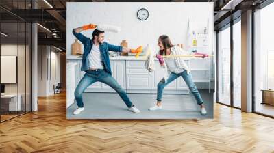 couple having fun and pretending fight with cleaning tools in kitchen Wall mural