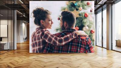 couple in checkered shirts looking at each other near christmas tree at home Wall mural