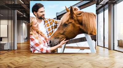 couple of smiling ranchers palming horse in stable Wall mural