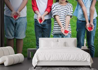 Cropped shot of cute little children holding red hearts while standing on green grass Wall mural