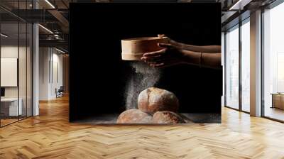 cropped shot of female baker sieving flour over various types of bread on sackcloth isolated on black background Wall mural