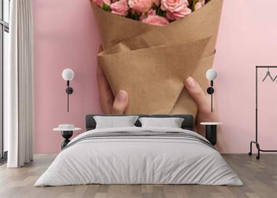 cropped shot of female hands holding bouquet of beautiful pink roses wrapped in craft paper on pink Wall mural