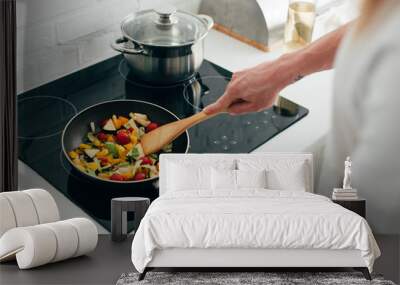 cropped shot of man cooking vegetables in frying pan on electric stove Wall mural