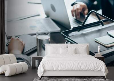 Cropped view of businesswoman holding pen near notebook and glass of water during consultation with investor on blurred background, banner Wall mural