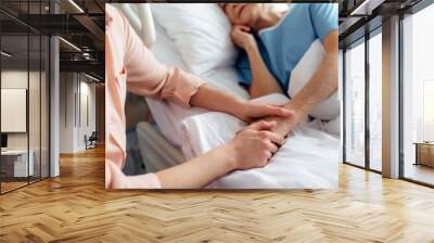 cropped view of daughter sitting near senior mother in bed and holding hands in hospital Wall mural