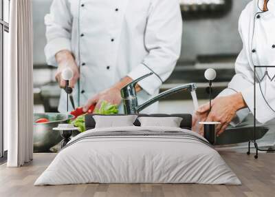 cropped view of female chef washing hands over sink while colleague cooking on background in restaurant kitchen Wall mural