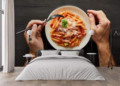 cropped view of man eating tasty bolognese pasta with tomato sauce and Parmesan from white plate on black wooden background Wall mural