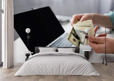 Cropped view of man holding dollar banknotes near laptop with blank screen on table, earning online concept Wall mural