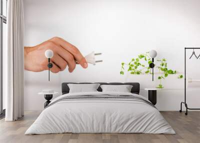 cropped view of man holding power plug near green plant growing in socket in power extender on white background Wall mural