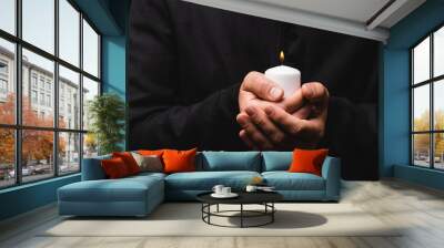 cropped view of priest holding burning candle in hands isolated on black Wall mural