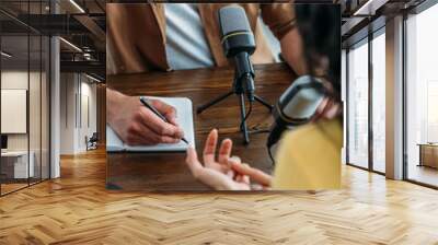 cropped view of radio host writing in notebook while interviewing woman in broadcasting studio Wall mural