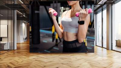 Cropped view of strong female doing dumbbells exercises in fitness gym Wall mural