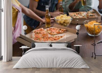 Cropped view of tasty pizza and potato chips on table near friends with beer on blurred background Wall mural