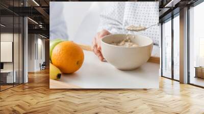 cropped view of woman eating oatmeal near fresh fruits and doctor on blurred background, banner Wall mural