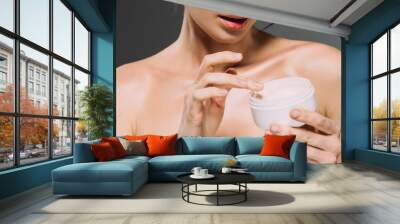 cropped view of woman holding plastic container with face cream isolated on grey Wall mural