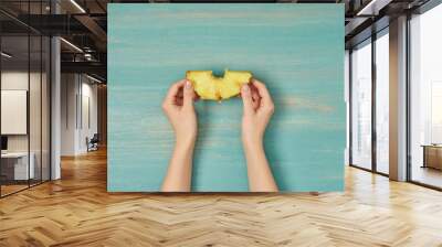 cropped view of woman holding yellow slice of pineapple on turquoise wooden table Wall mural