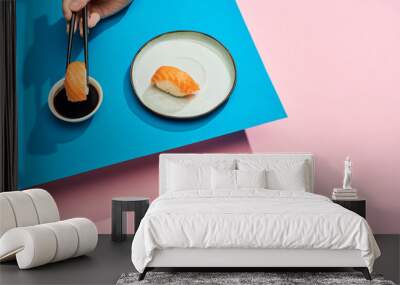 cropped view of woman putting fresh nigiri with salmon into soy sauce on blue, pink background Wall mural