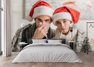 diseased couple wearing santa hats and covered with blanket looking at camera Wall mural