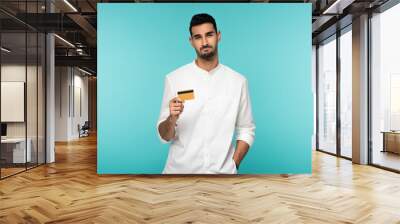 Displeased muslim man with credit card looking at camera isolated on blue Wall mural