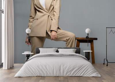 elegant woman in beige suit posing near wooden chair and looking away on grey Wall mural