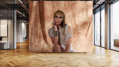 Elegant woman in egyptian headdress and pearl top looking at camera on abstract background Wall mural