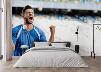 emotional professional soccer player in blue and white uniform showing yes gesture at stadium, panoramic shot Wall mural