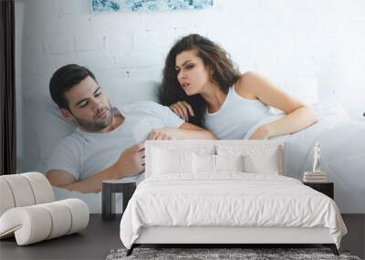 emotional young woman looking at boyfriend using smartphone in bed, relationship difficulties concept Wall mural