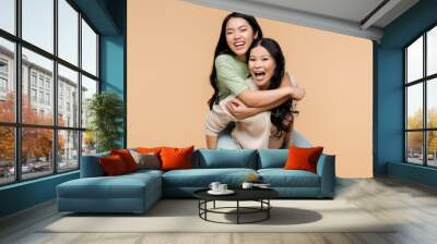 excited asian mother piggybacking happy young adult daughter isolated on beige, banner Wall mural