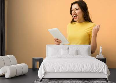 Excited brunette girl holding digital tablet and laughing isolated on orange Wall mural