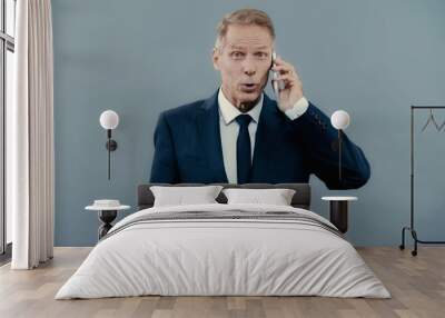 Excited businessman talking on smartphone and looking at camera isolated on grey. Wall mural