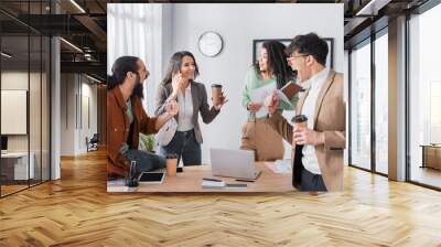 Excited hispanic co-workers looking at female colleague talking on mobile phone near workplace Wall mural