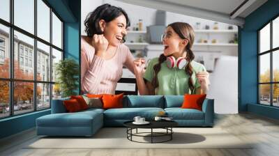 Excited hispanic mother and daughter with yes gesture looking at each other during online studying in kitchen on blurred foreground Wall mural