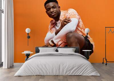 Fashionable African American man in stylish attire crouching on vivid orange background. Wall mural