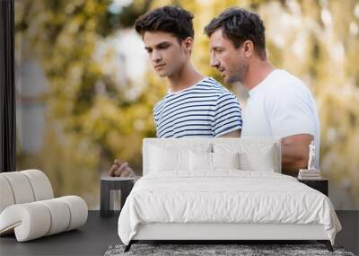 father gesturing and talking with teenager son in park Wall mural