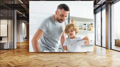 father with son whisking eggs in bowl at kitchen Wall mural