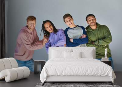 four cheerful men in casual outfits smiling at camera posing on grey backdrop, cultural diversity Wall mural