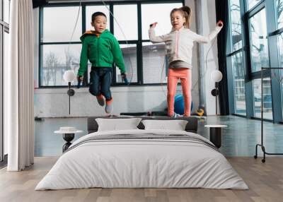 Front view of multicultural children doing exercise with jump rope in gym Wall mural