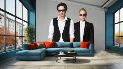 front view of young couple in dark sunglasses and black and white clothing isolated on grey Wall mural