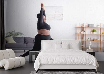 full length of cheerful african american plus size woman in sportswear standing in yoga pose in living room Wall mural