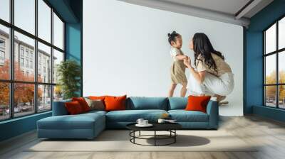 full length of happy asian toddler kid holding hands with stylish mother on grey Wall mural