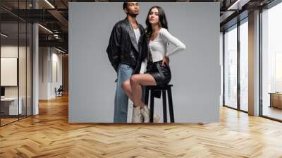 full length of woman in leather skirt sitting on high chair near stylish african american man on grey. Wall mural