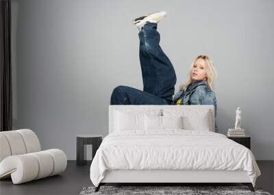 full length of young blonde model in denim outfit and trendy sneakers posing on grey. Wall mural