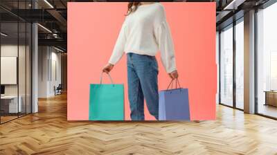 full length view of woman in white sweater and jeans holding shopping bags on pink background Wall mural