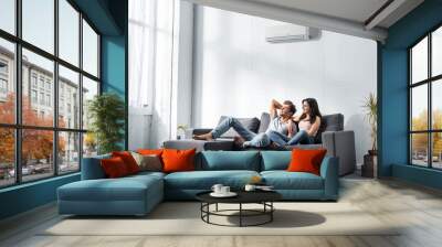 Girlfriend and handsome boyfriend sitting on sofa and looking away Wall mural