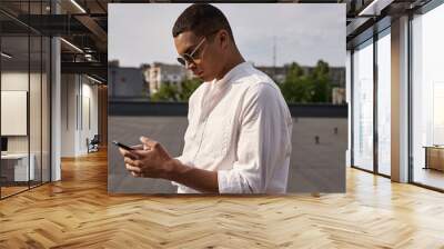 good looking young african american man in casual attire with sunglasses looking at smartphone Wall mural