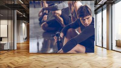 group of athletic young people in sportswear sitting on floor and resting at the gym, group fitness concept Wall mural