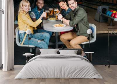 group of friends clinking mugs of beer at bowling club in front of alleys Wall mural