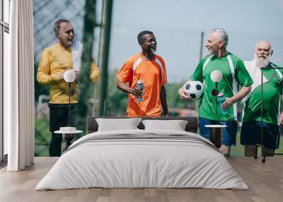 group of interracial elderly sportsmen with sportive water bottles walking on football field Wall mural