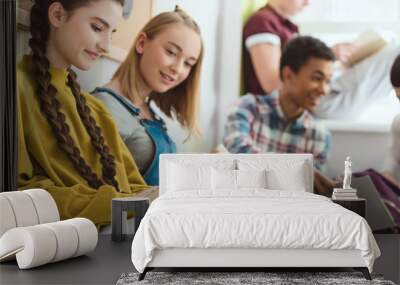 Group of smiling multicultural teenage schoolchildren reading books during school break Wall mural